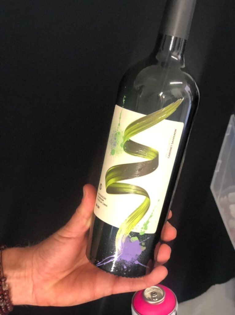 Garrafa de vinho com rótulo pintado à mão, segurada sobre fundo preto