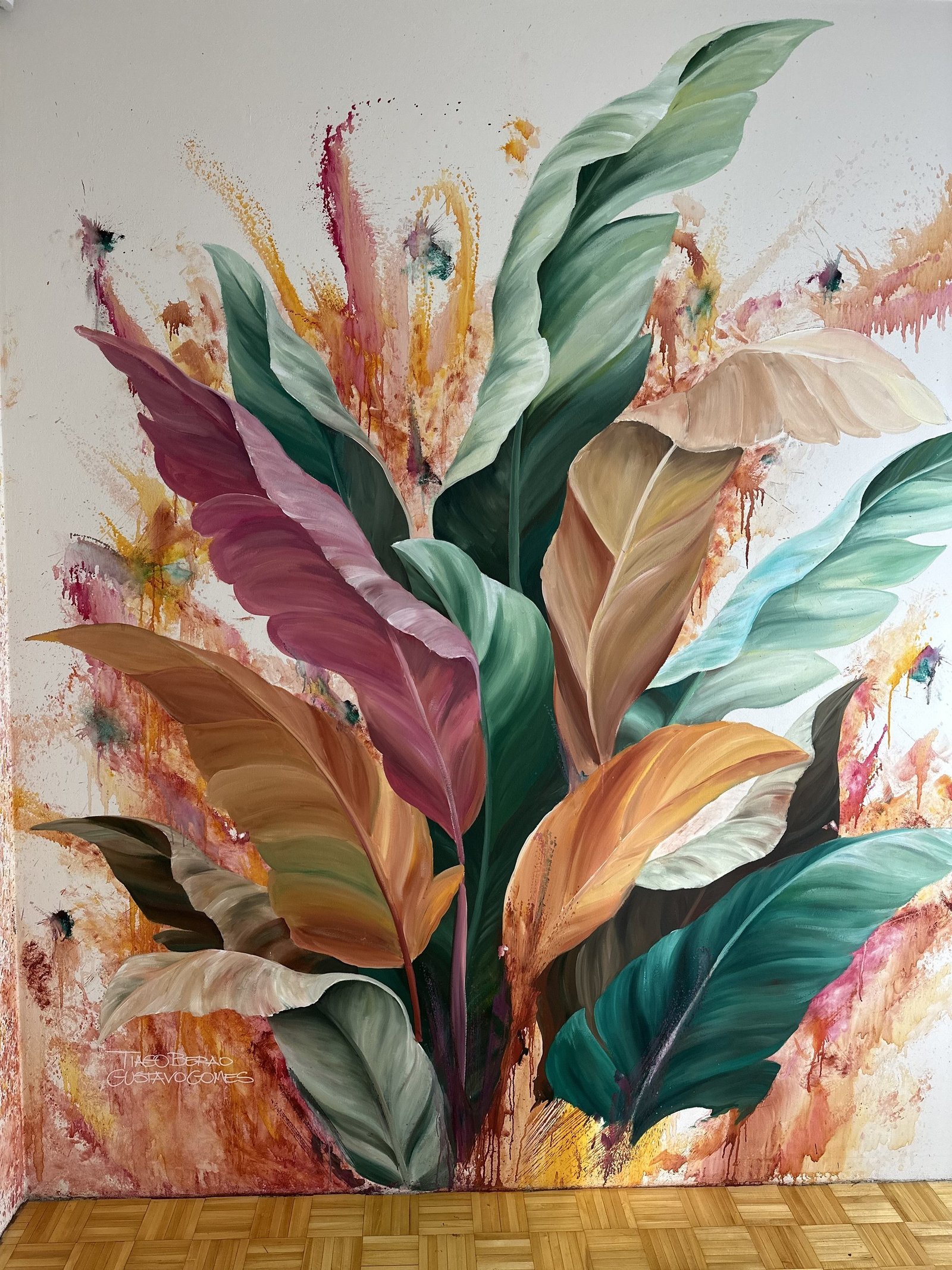 Folhas tropicais em verde, rosa, laranja e creme pintadas sobre parede branca