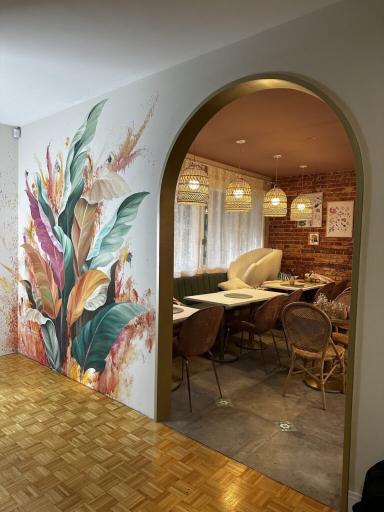 O mural ao lado do arco de entrada que leva ao salão com mesas e luminárias