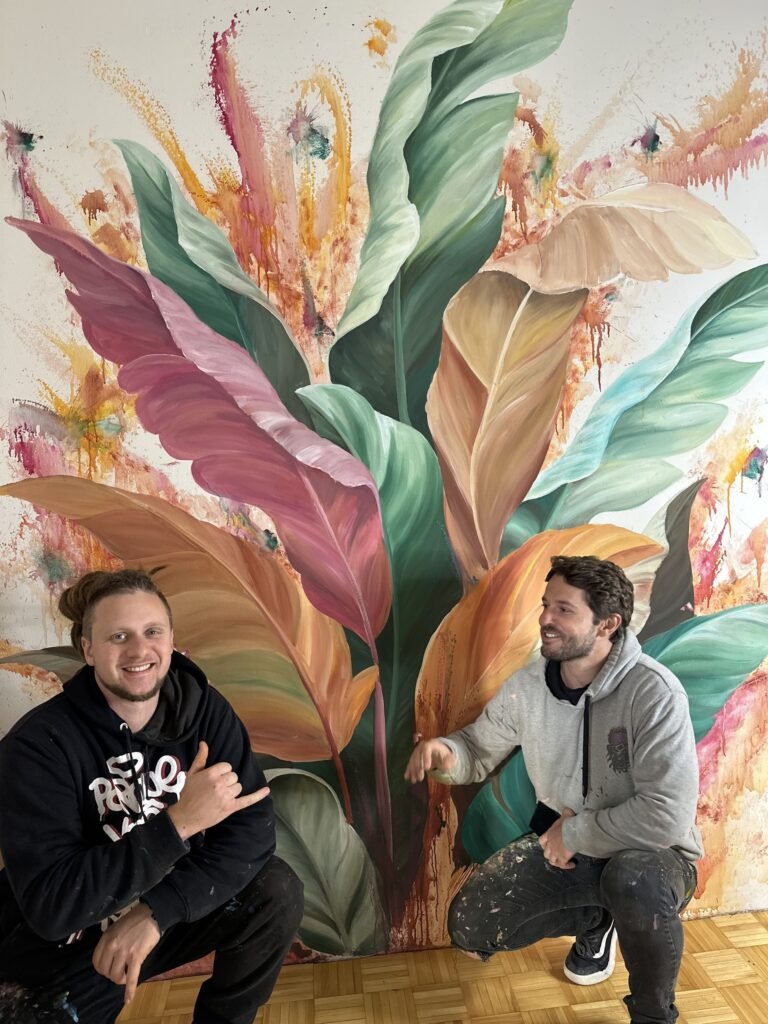 Dois artistas agachados em frente ao mural pronto