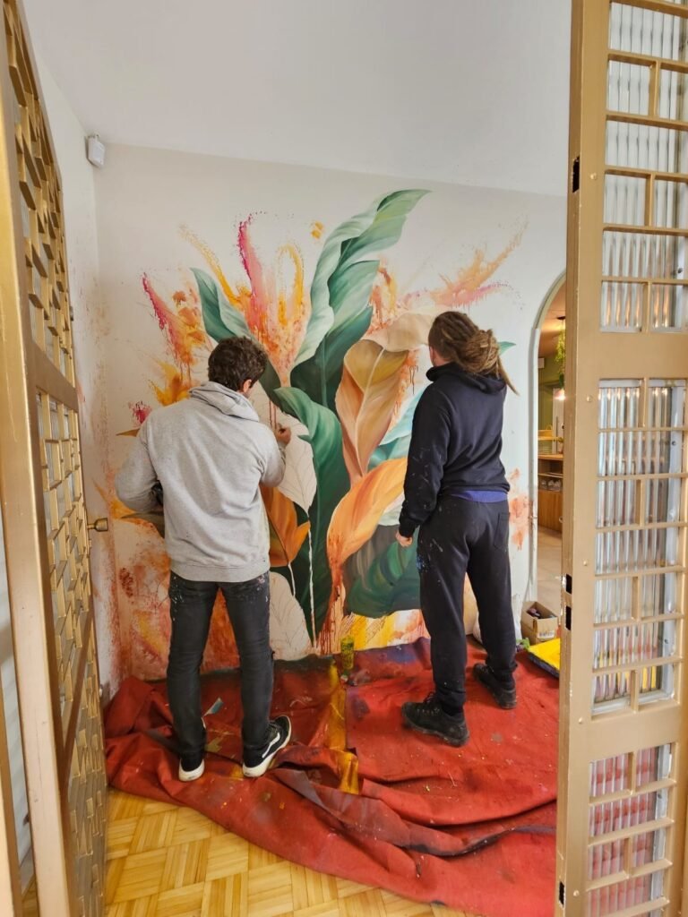Duas pessoas pintando a parede, com o piso protegido por uma lona vermelha