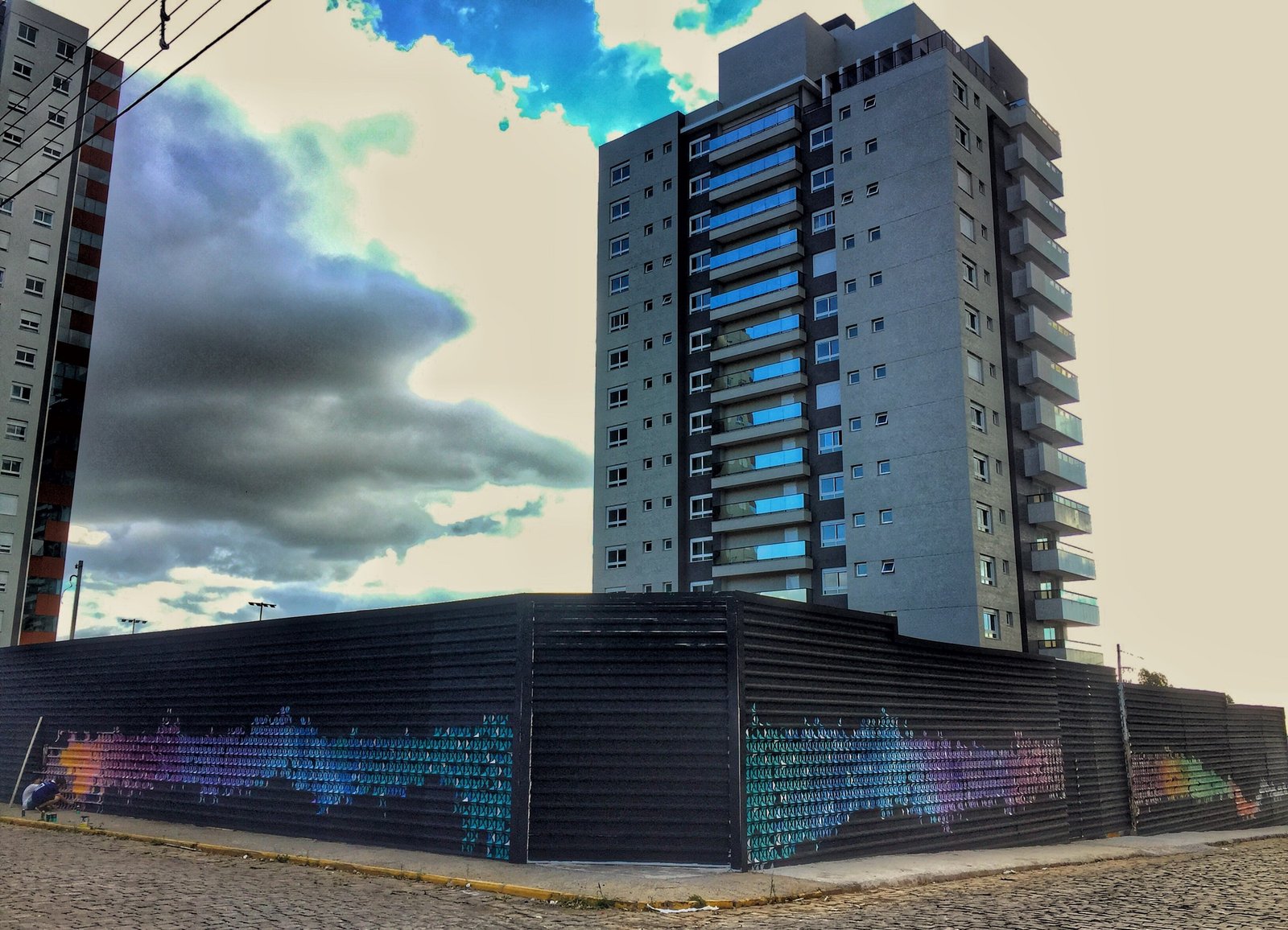 Tapume preto pintado com um degradê colorido em volta do terreno, com o prédio ao fundo
