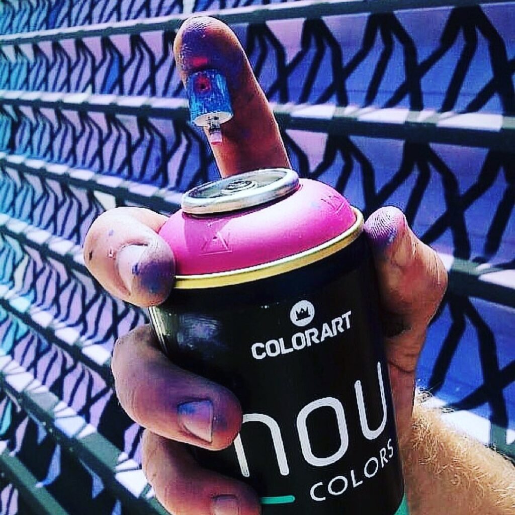Mão com lata de spray rosa em frente ao tapume pintado