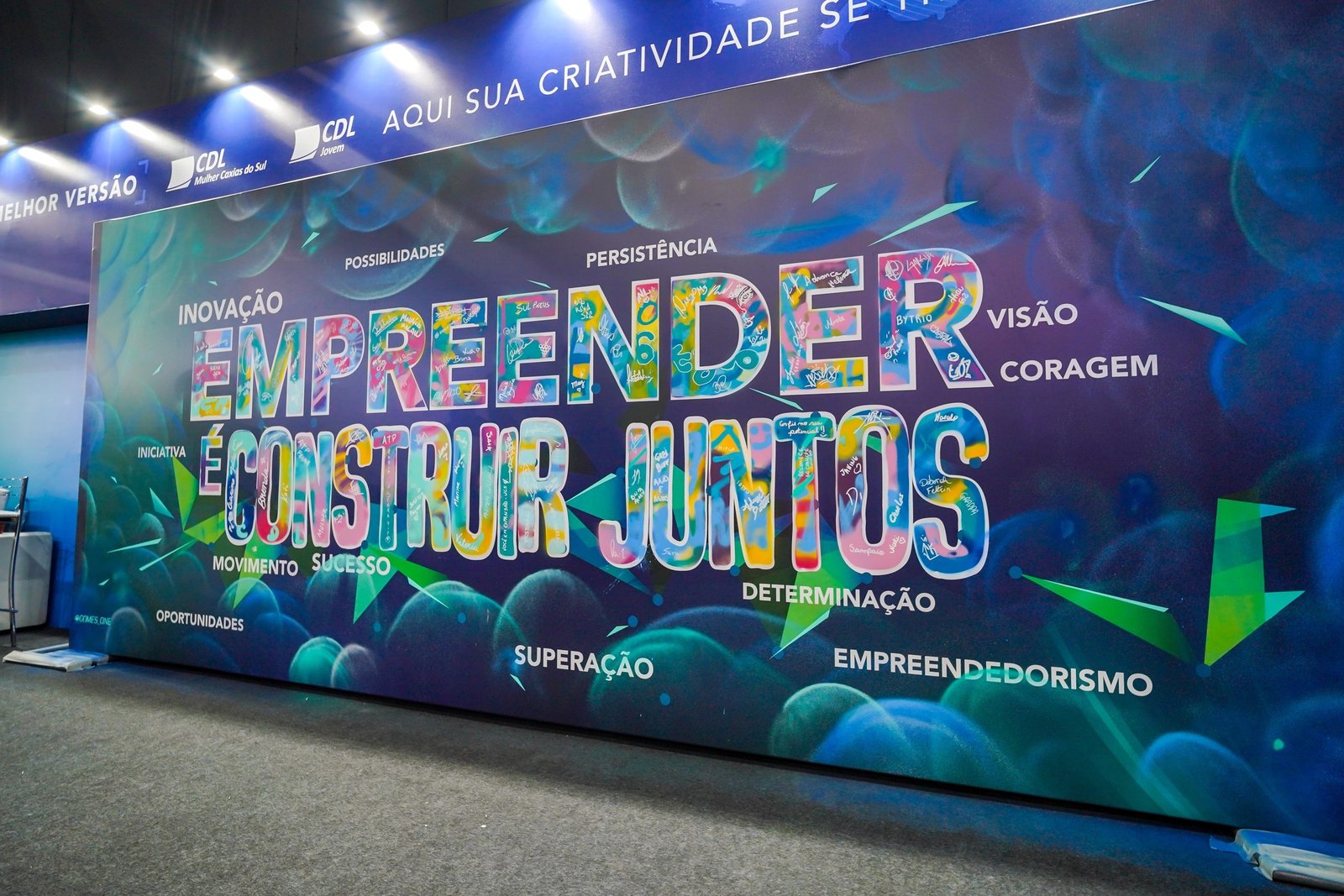 A parede pronta no estande da CDL com a frase empreender é construir juntos em letras coloridas