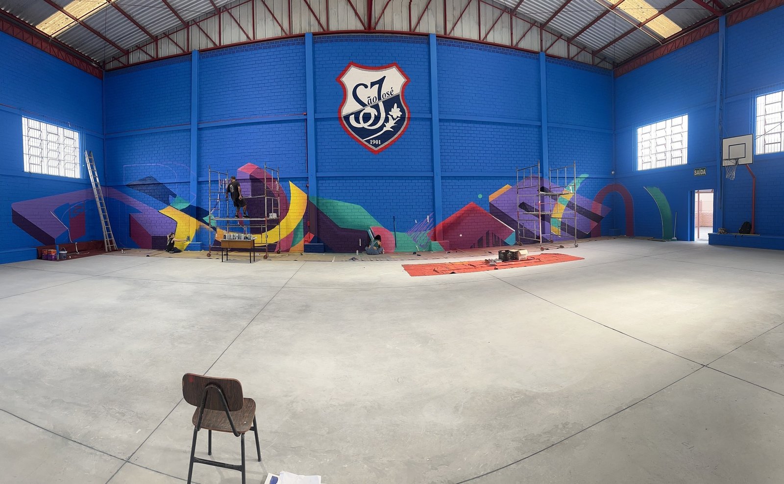 O ginásio do Colégio São José com a parede azul pintada e o brasão do colégio no alto