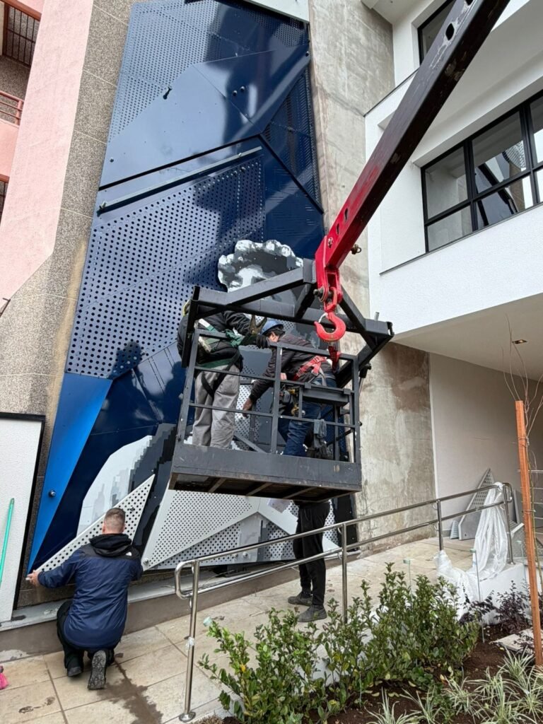 Peça sendo fixada na fachada a partir do cesto do guindaste