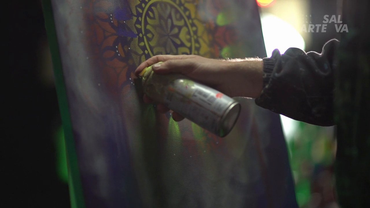 Mão com lata de spray pintando uma mandala colorida sobre tela