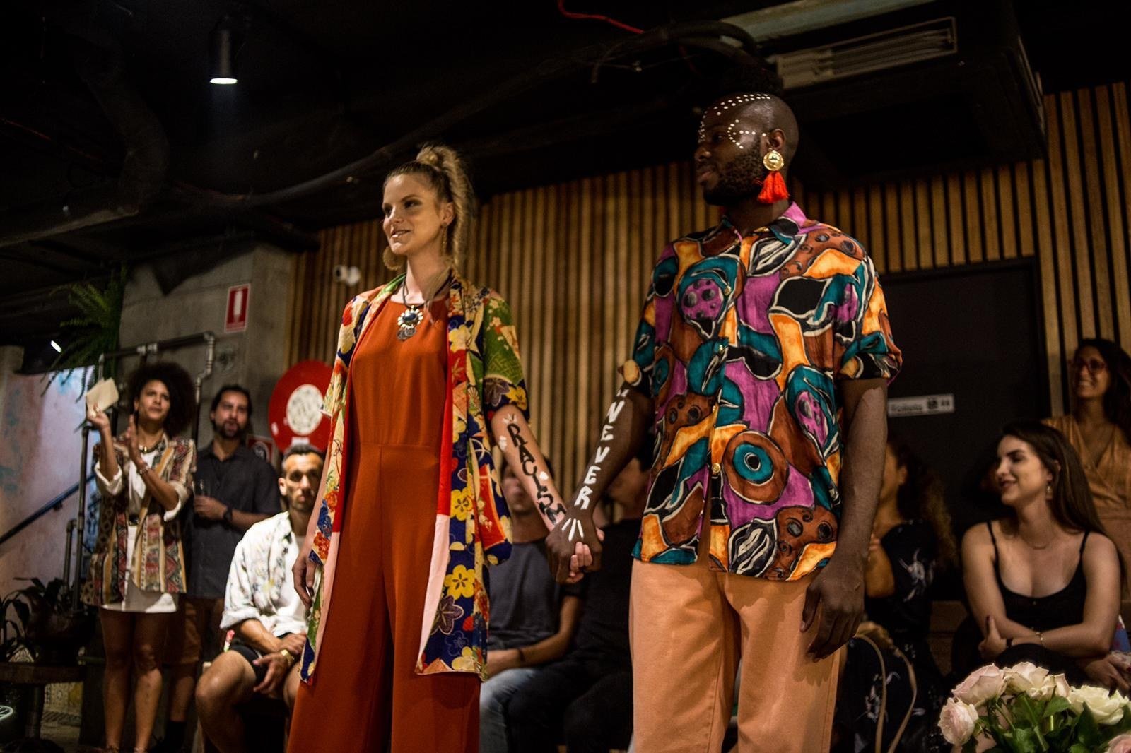Dois modelos na passarela com roupas estampadas pintadas à mão, diante do público