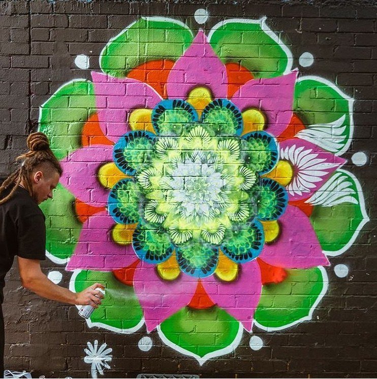 Mandala rosa, verde e laranja pintada com spray num muro de tijolos escuros