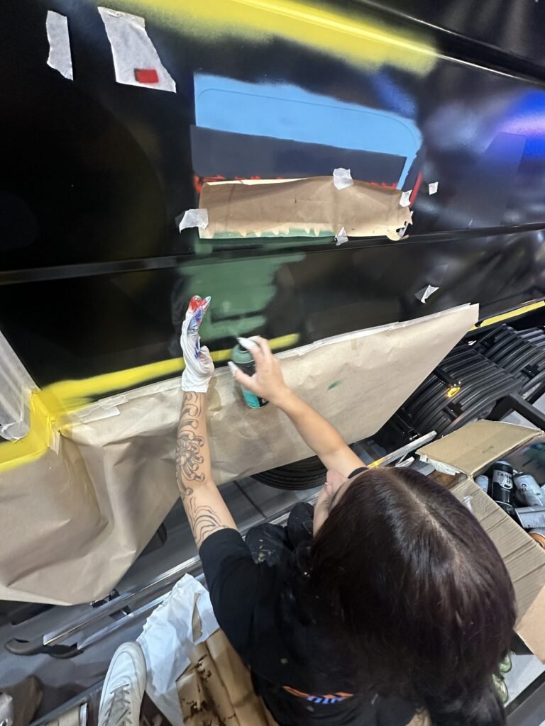 Integrante da equipe pintando uma letra com spray, com o resto protegido por papel