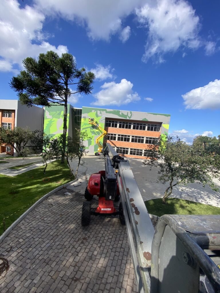 A fachada pintada vista de longe, entre as árvores do campus