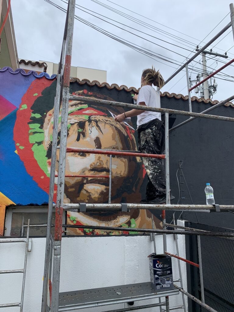 Integrante da equipe no andaime pintando o retrato da criança