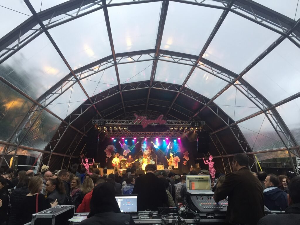 Palco do festival sob uma tenda de vidro, com o público em frente