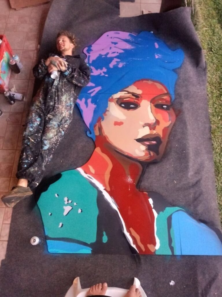 A figura sendo pintada deitada no chão, sobre uma lona