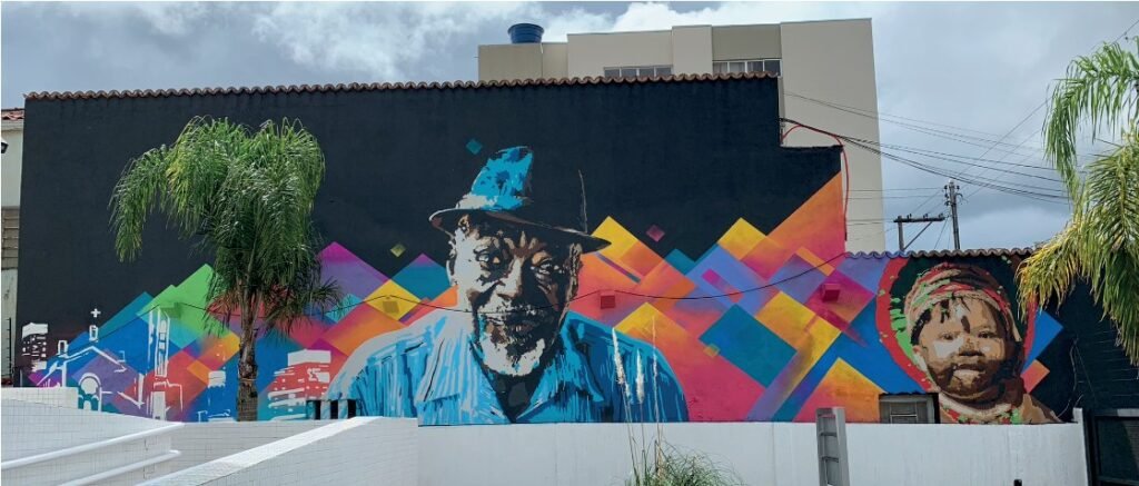 Paredão da sede do Ministério Público Federal coberto por grafite geométrico colorido, com um rosto ao centro