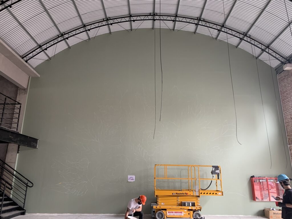 A parede verde-oliva ainda vazia, com a plataforma no chão do galpão