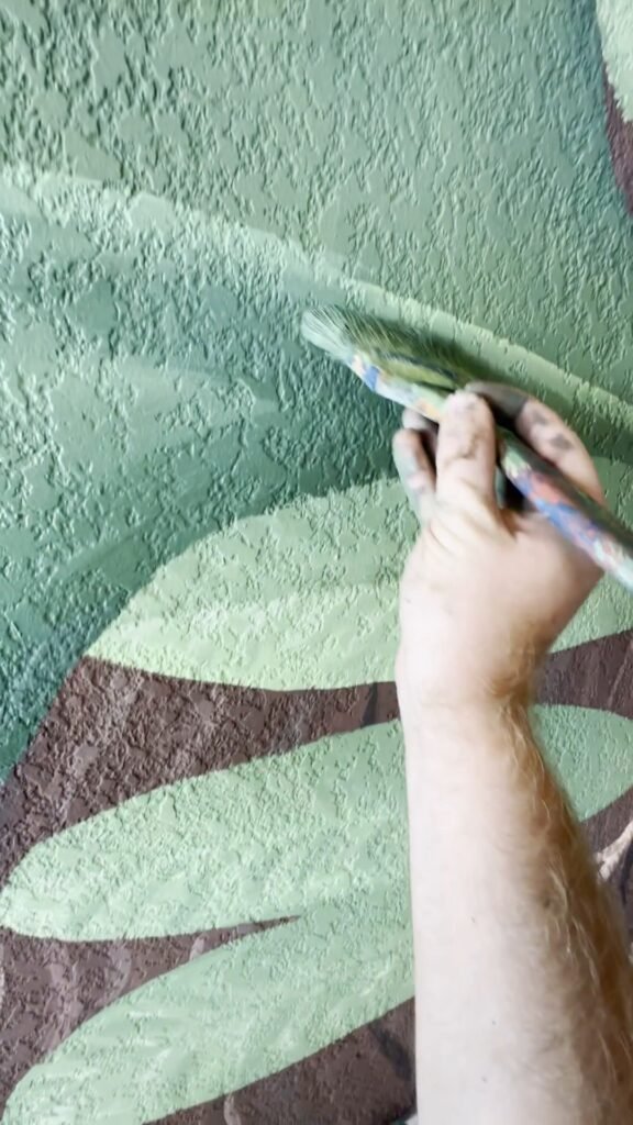 Mão pintando uma folha com pincel, com os potes de tinta ao lado