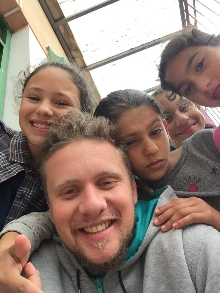 Gustavo Gomes sorrindo numa selfie com crianças da oficina