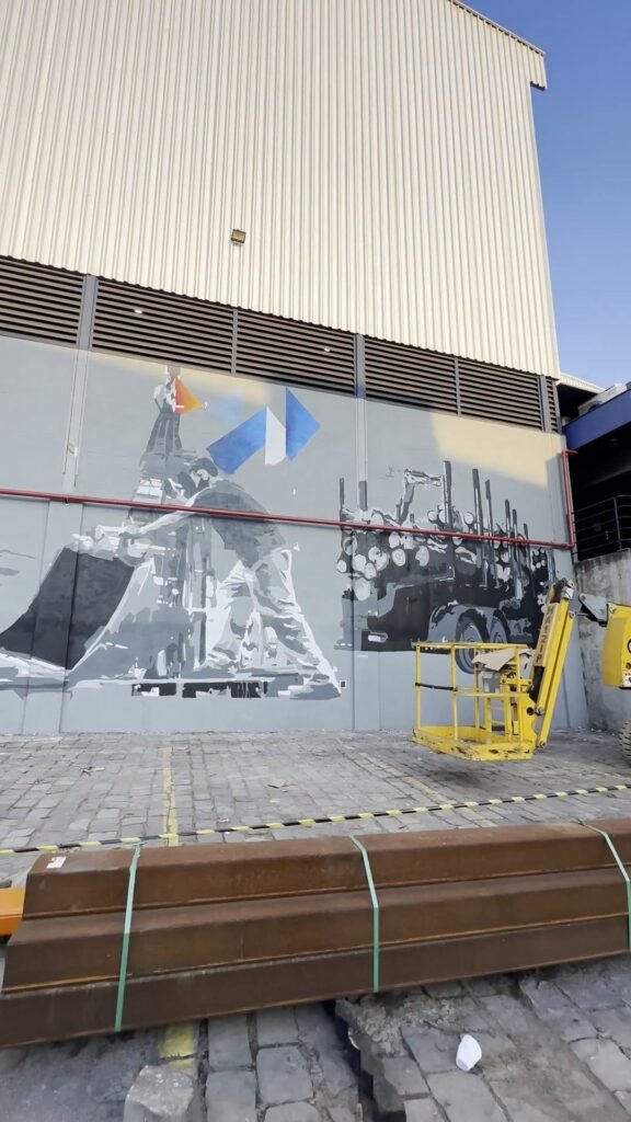 Mural em cinza de um operário e uma máquina na parede externa do galpão