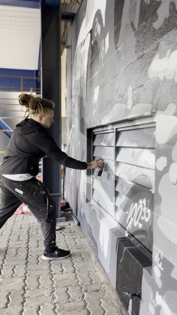 Integrante da equipe pinta com spray o mural cinza da parede externa