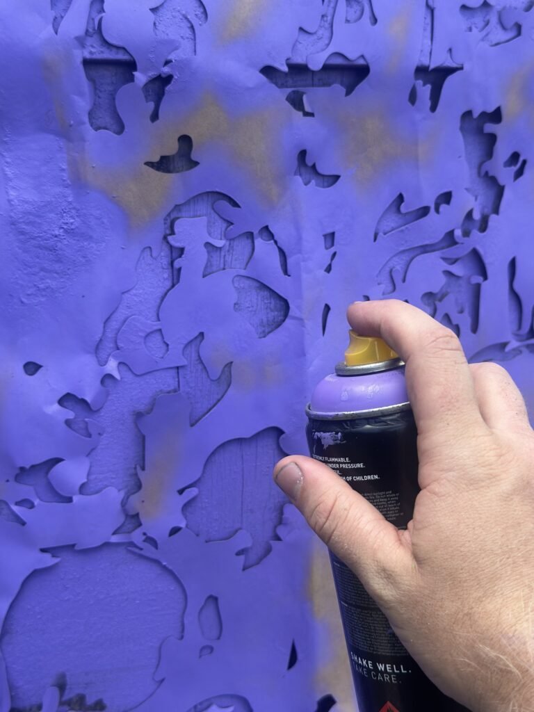 Mão com lata de spray roxa pintando sobre a madeira