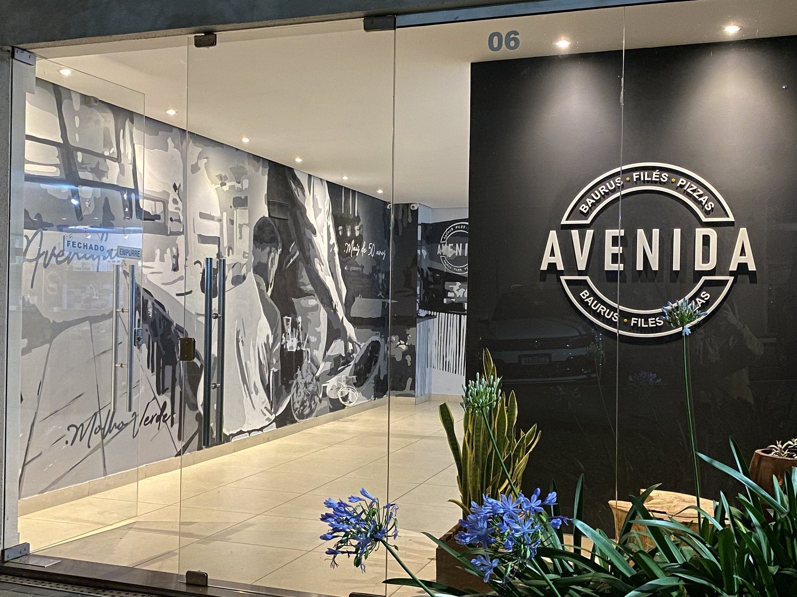 Entrada do Avenida com o letreiro e o mural em preto e branco atrás do vidro