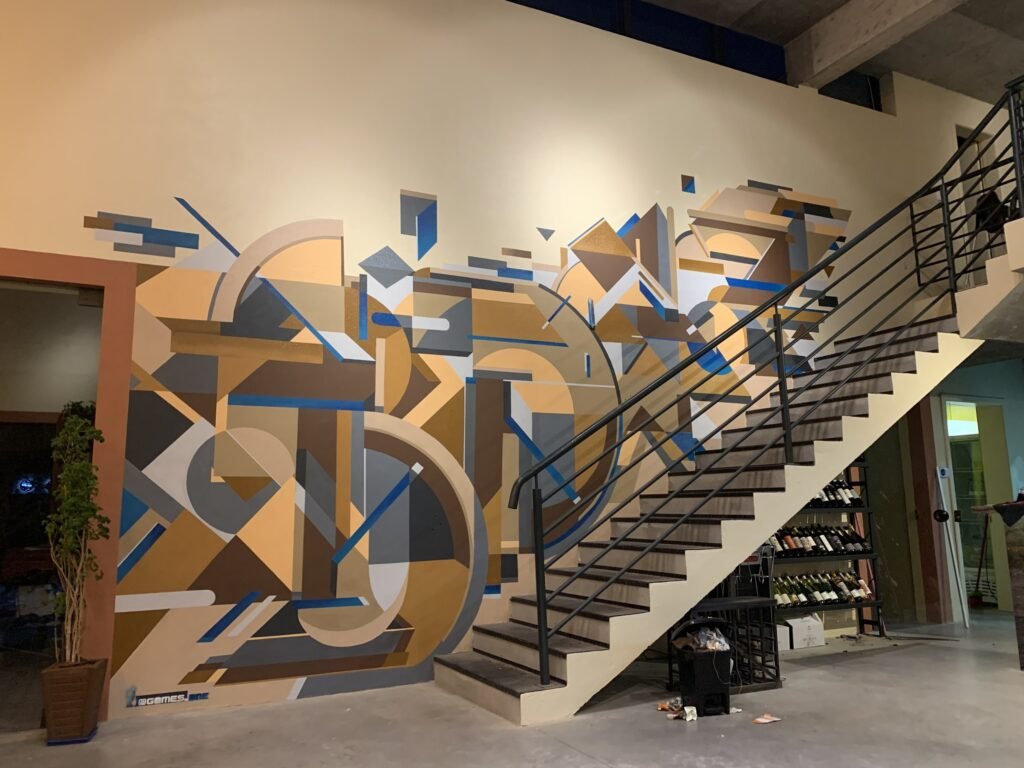 Escada do Boaz com a parede coberta de planos geométricos em laranja, cinza e azul