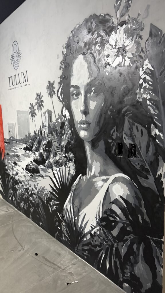Retrato de mulher em preto e branco entre folhagens, ao lado do nome Tulum