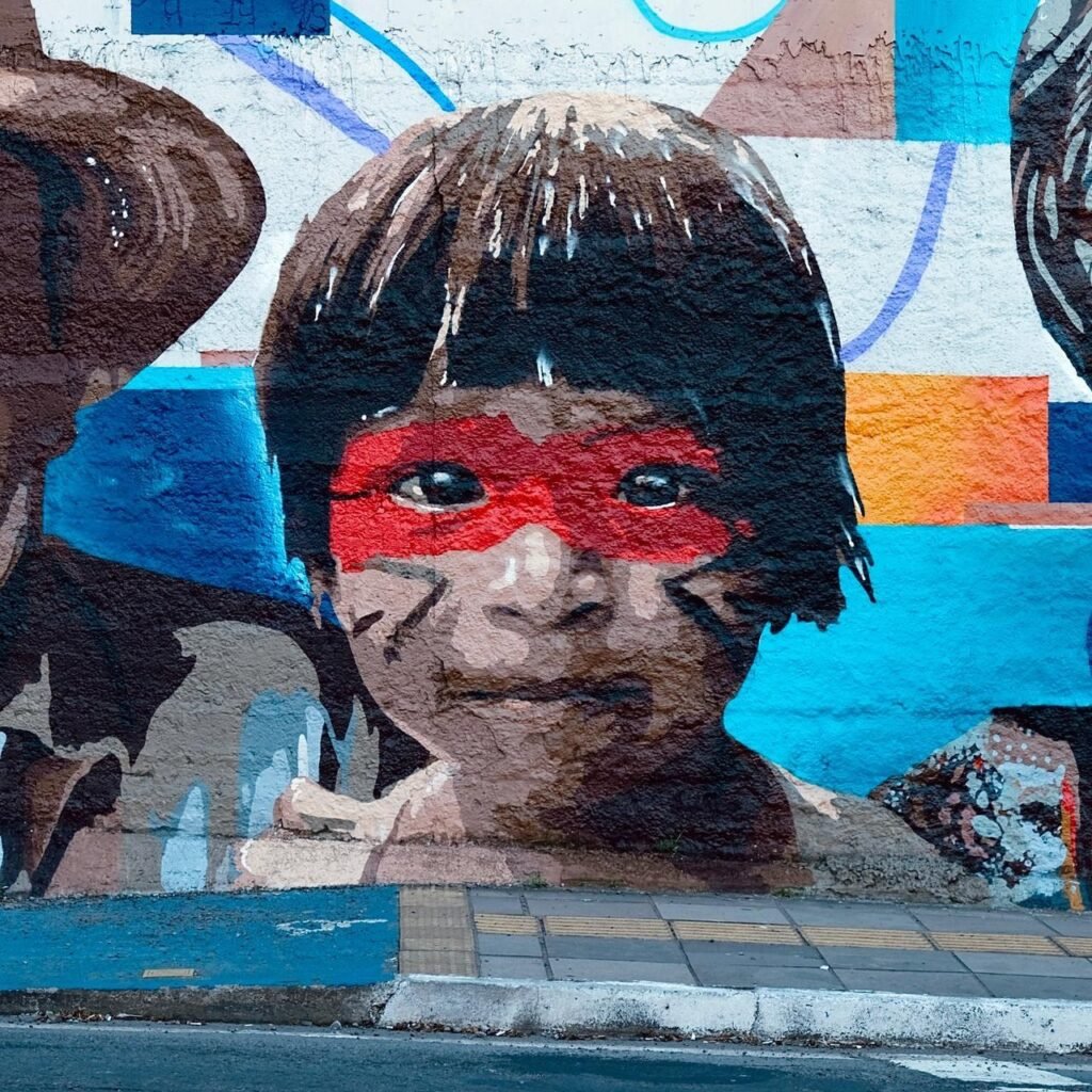 Retrato de uma criança com pintura facial vermelha, sobre fundo azul e laranja