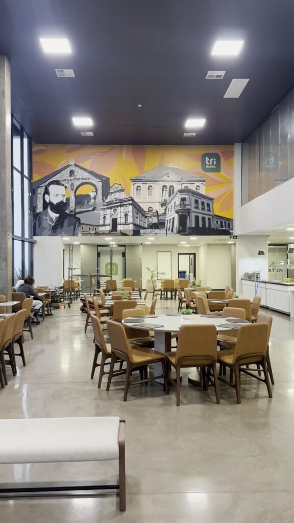 Salão de refeições do Tri Hotel Antônio Prado, com o mural no alto da parede do fundo