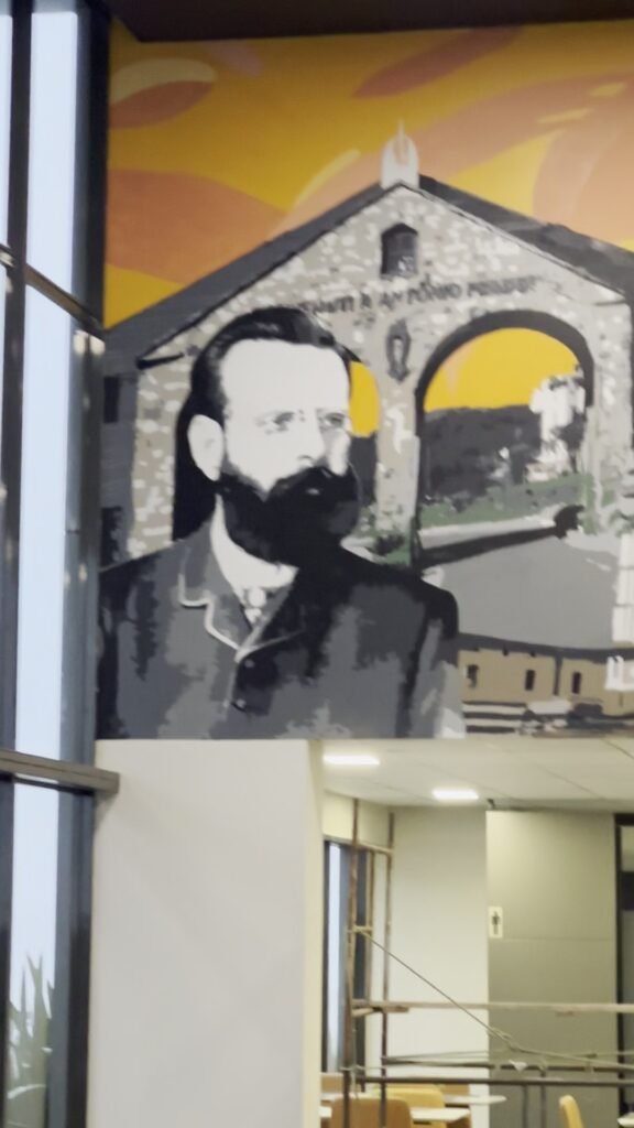 Retrato em preto e branco de um homem de barba diante de uma construção com porta em arco