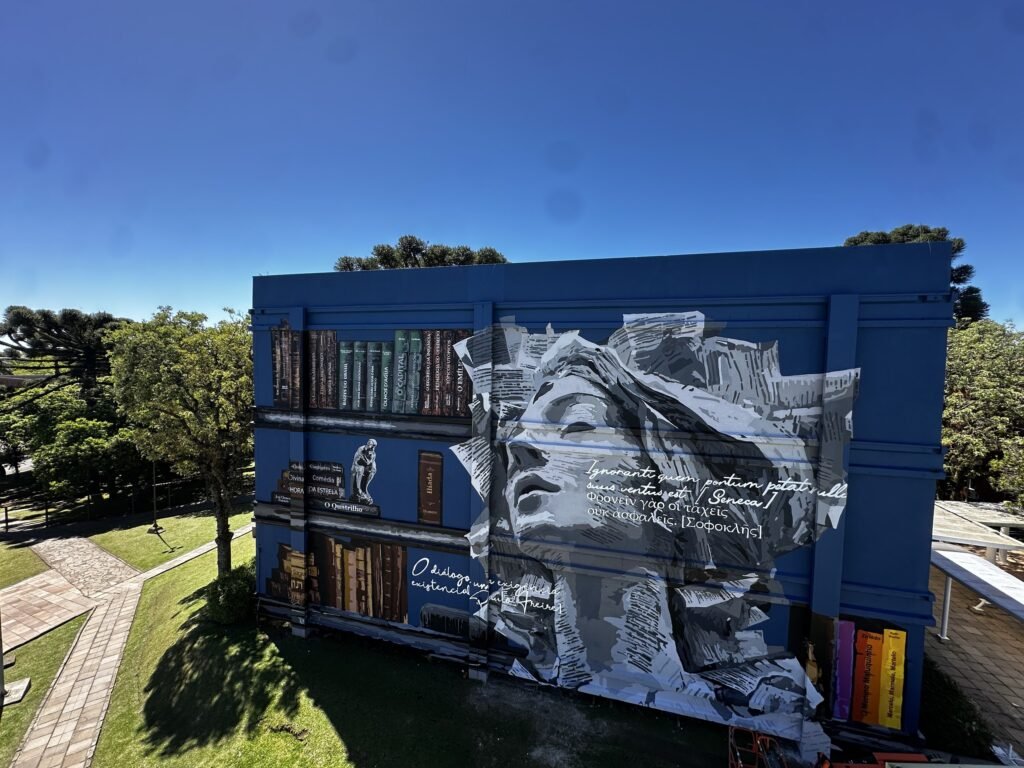 O mural pronto, com o rosto que se desfaz em páginas ao lado da estante